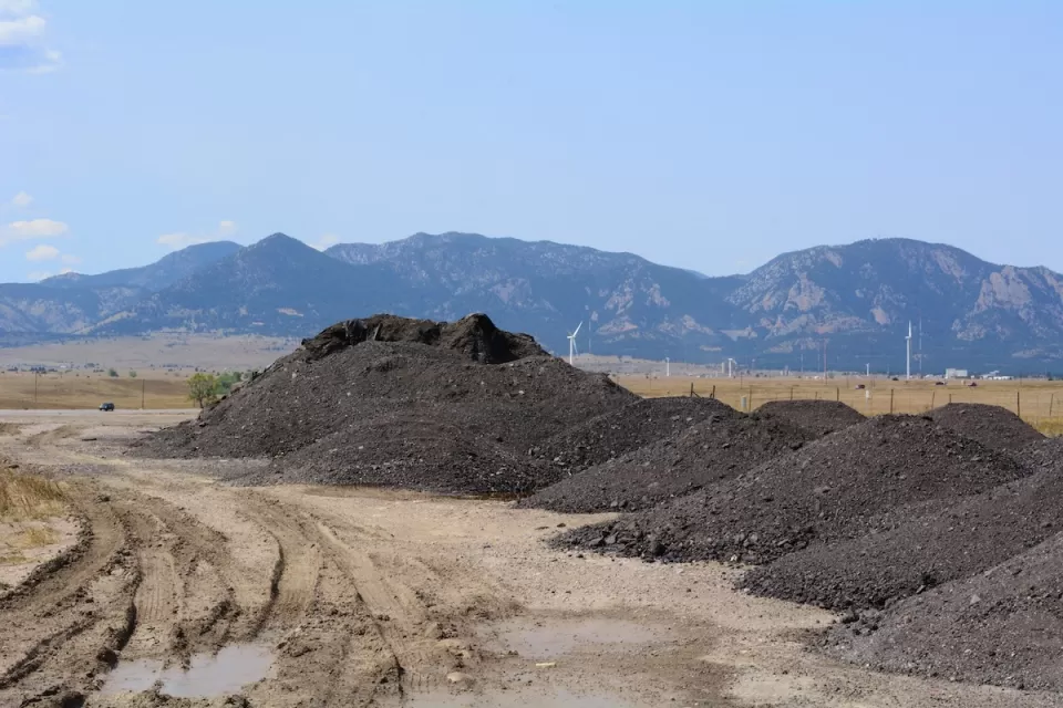 Piles of recycled asphalt and bitumen to be recycled for making roads with Rocky Mountains in background.